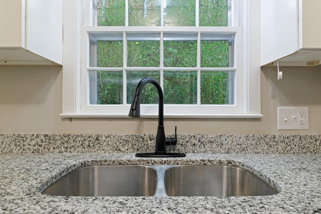 room details with white cabinets, light stone countertops, and sink