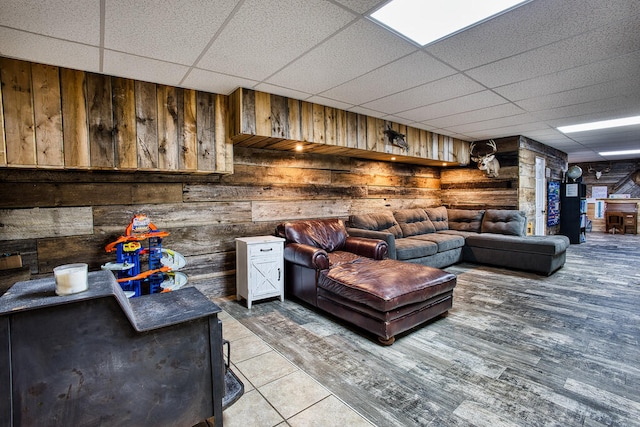 living room featuring tile patterned flooring, a paneled ceiling, and wooden walls