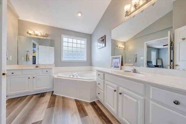 bathroom featuring tiled bath, vanity, hardwood / wood-style flooring, and vaulted ceiling