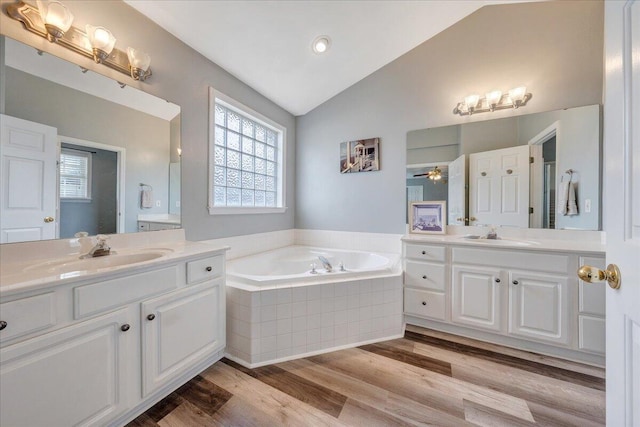 bathroom featuring hardwood / wood-style floors, vanity, lofted ceiling, ceiling fan, and tiled tub