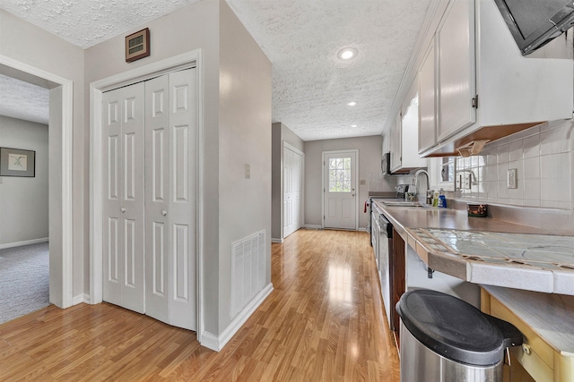 kitchen featuring sink, tile counters, a textured ceiling, white cabinets, and light wood-type flooring