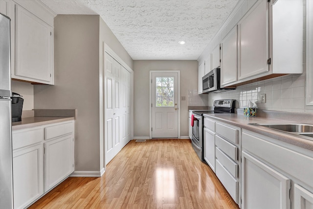 kitchen featuring white cabinets, light hardwood / wood-style floors, a textured ceiling, and appliances with stainless steel finishes