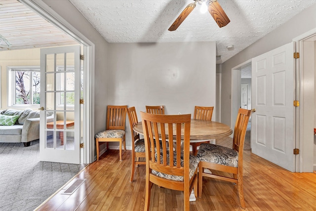 dining area featuring ceiling fan, light wood-type flooring, a textured ceiling, and french doors