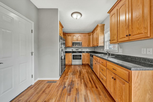 kitchen with dark stone counters, sink, appliances with stainless steel finishes, and light hardwood / wood-style flooring