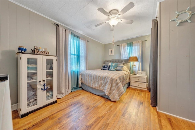 bedroom with french doors, ceiling fan, wooden walls, crown molding, and light hardwood / wood-style floors