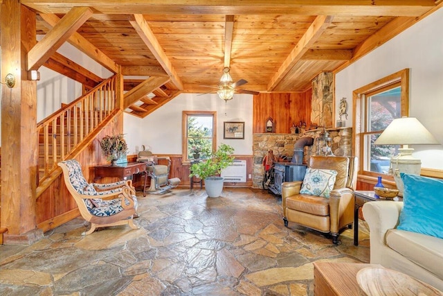 living area featuring a wood stove, stone flooring, wooden ceiling, wainscoting, and stairs