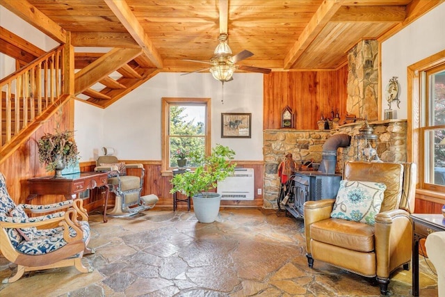 sitting room featuring a wood stove, stone floors, a healthy amount of sunlight, and wood ceiling