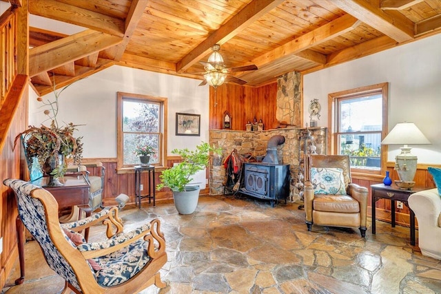 sitting room with stone floors, wood ceiling, a wood stove, and wainscoting