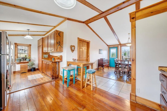 kitchen featuring lofted ceiling with beams, hanging light fixtures, stainless steel refrigerator, and light hardwood / wood-style flooring