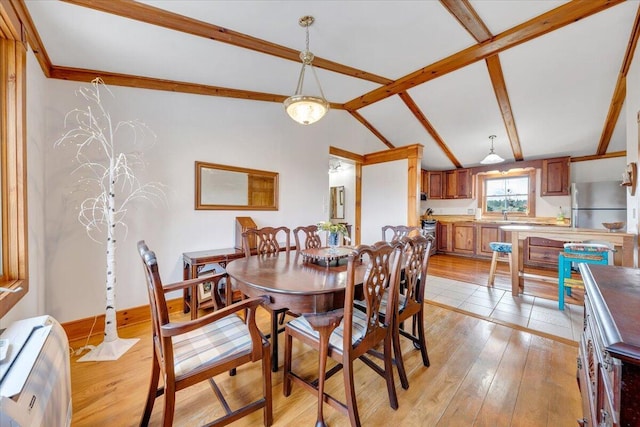 dining area with light wood finished floors, lofted ceiling with beams, and baseboards