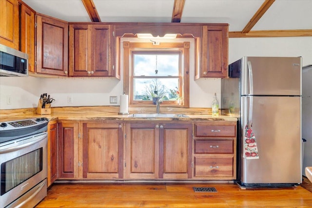 kitchen featuring beam ceiling, sink, stainless steel appliances, and light wood-type flooring