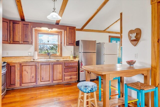 kitchen featuring light hardwood / wood-style flooring, beamed ceiling, stainless steel appliances, and decorative light fixtures