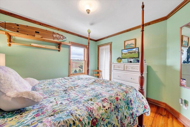 bedroom with hardwood / wood-style floors, crown molding, baseboards, and a closet