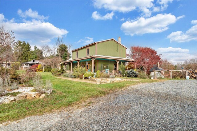 view of side of property featuring a porch, a lawn, gravel driveway, and a chimney