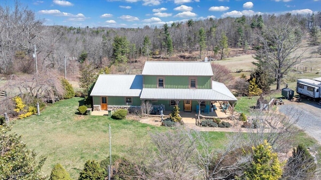 view of front facade featuring a porch, a forest view, metal roof, and a front lawn