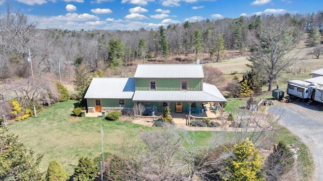 view of front of home with covered porch, a forest view, metal roof, a front lawn, and driveway