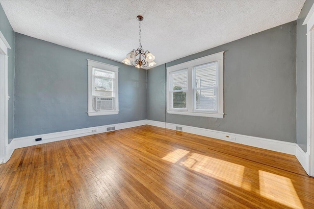 unfurnished room with a notable chandelier, cooling unit, a textured ceiling, and hardwood / wood-style flooring