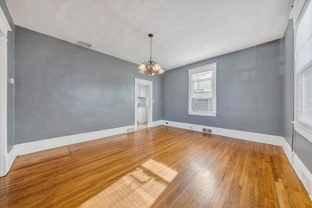 empty room featuring hardwood / wood-style floors, a textured ceiling, an inviting chandelier, and cooling unit