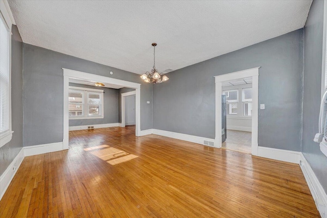 unfurnished living room featuring a notable chandelier, wood-type flooring, and a textured ceiling