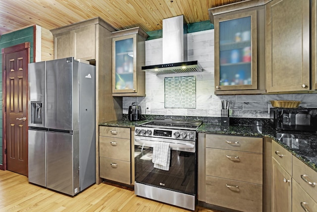 kitchen featuring wall chimney range hood, light wood-type flooring, dark stone counters, and appliances with stainless steel finishes