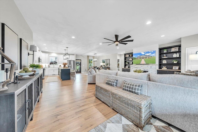 living room featuring ceiling fan with notable chandelier and light hardwood / wood-style flooring