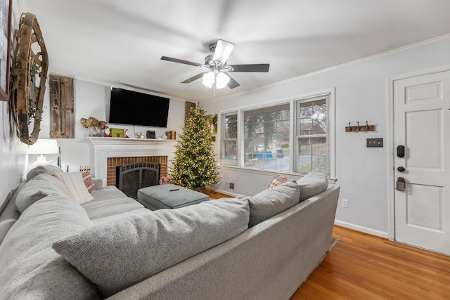 living room with crown molding, ceiling fan, a fireplace, and light wood-type flooring