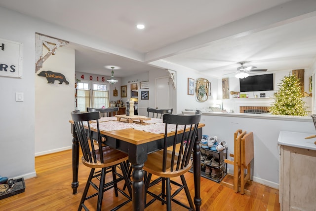 dining room with a brick fireplace, ceiling fan, and light hardwood / wood-style flooring