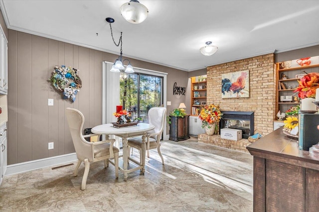 dining area with built in shelves, wood walls, crown molding, and a brick fireplace