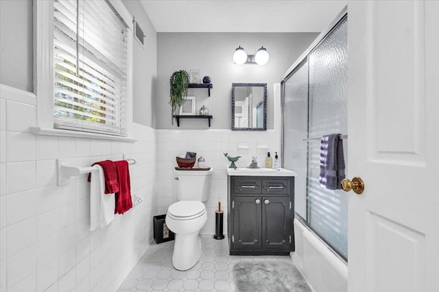 full bathroom featuring combined bath / shower with glass door, vanity, toilet, and tile walls