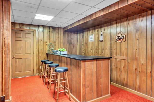 bar featuring carpet, a paneled ceiling, and wood walls