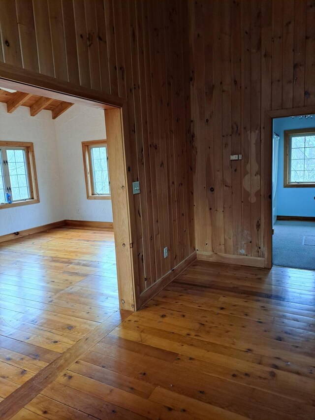 hall featuring beamed ceiling, wood walls, wood finished floors, and a notable chandelier