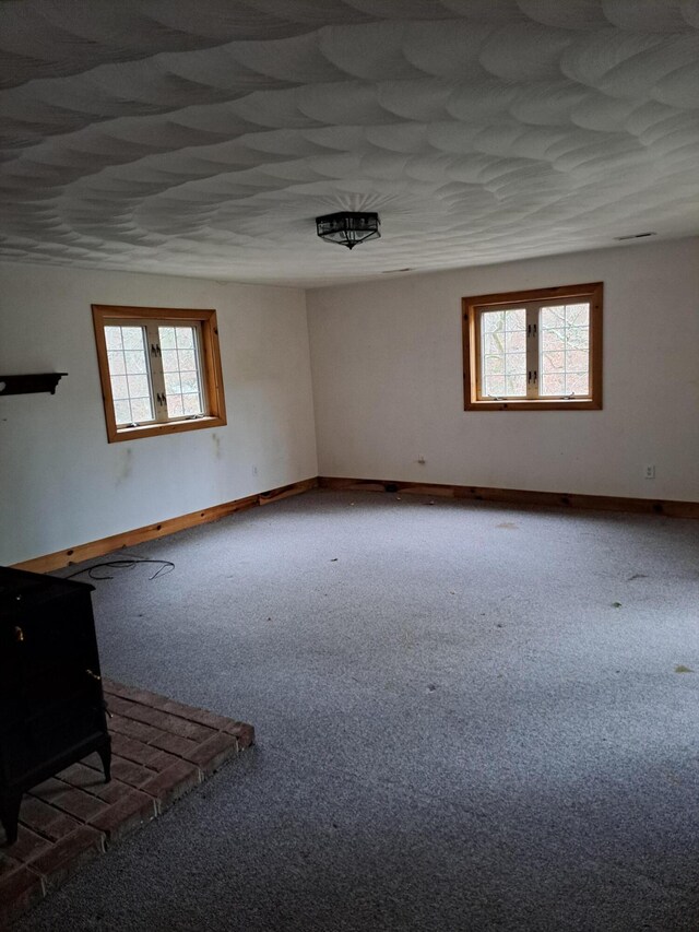 unfurnished living room with a wood stove, carpet flooring, wooden walls, and baseboards