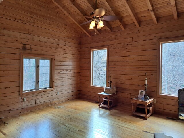 spare room with ceiling fan, vaulted ceiling with beams, wood walls, and wood finished floors