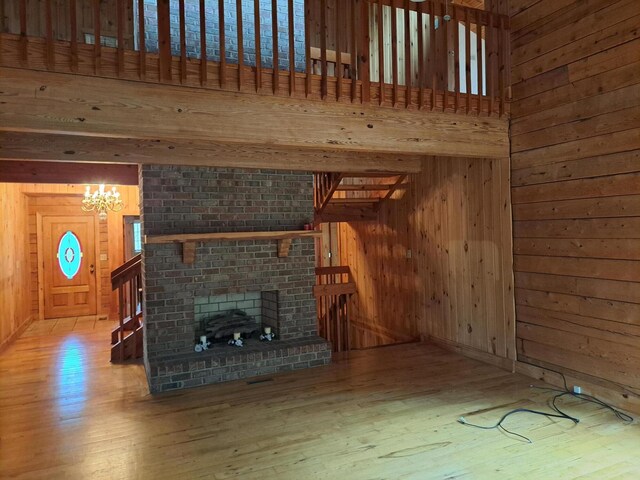 unfurnished living room with a chandelier, wood walls, wood finished floors, visible vents, and beamed ceiling