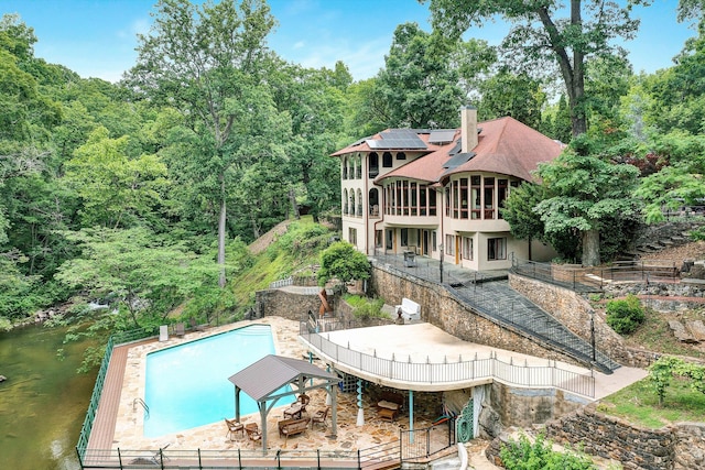 rear view of property with solar panels and a fenced in pool