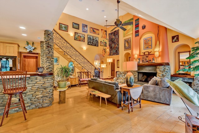 living room featuring a fireplace, a towering ceiling, light hardwood / wood-style flooring, and ceiling fan