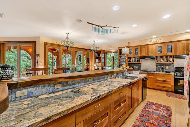 kitchen with light stone countertops, sink, hanging light fixtures, tasteful backsplash, and light wood-type flooring