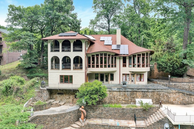 back of property with solar panels and a balcony