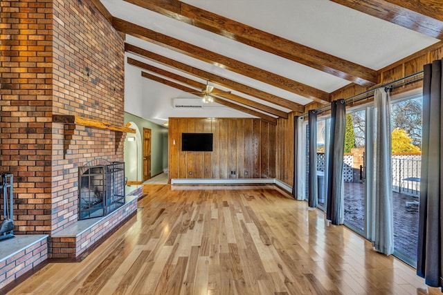 unfurnished living room with ceiling fan, a wall mounted air conditioner, a brick fireplace, high vaulted ceiling, and wooden walls