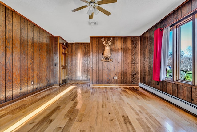 spare room featuring ceiling fan, wood-type flooring, baseboard heating, and wooden walls