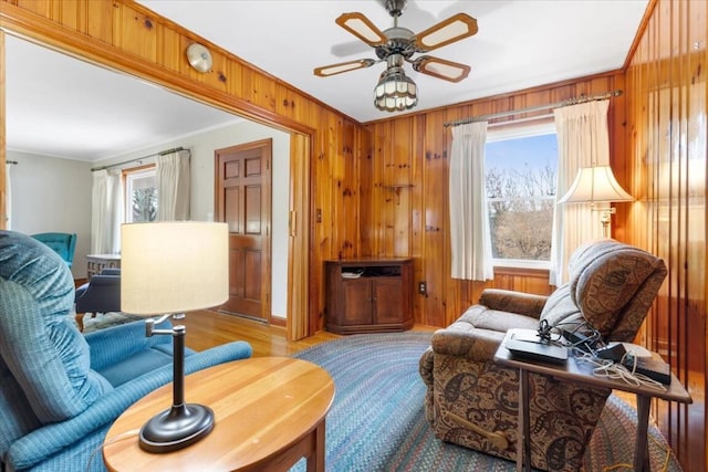 living room with a wealth of natural light, wooden walls, ceiling fan, and ornamental molding