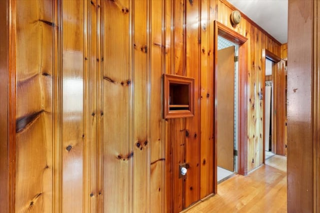 hallway featuring light wood-type flooring and wood walls