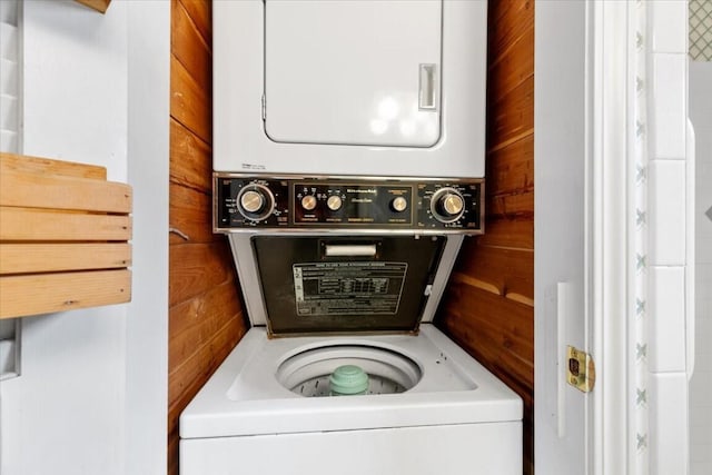 laundry area featuring wood walls and stacked washer / dryer