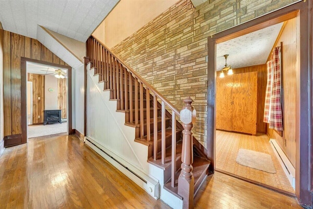 stairs featuring hardwood / wood-style floors, wooden walls, baseboard heating, and lofted ceiling