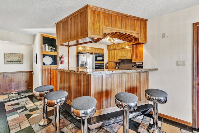 kitchen featuring black appliances, kitchen peninsula, a textured ceiling, and light tile patterned floors