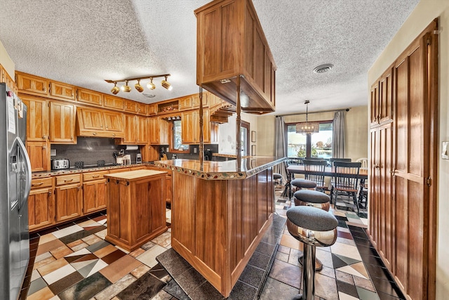 kitchen with stainless steel refrigerator with ice dispenser, a center island, a textured ceiling, and pendant lighting