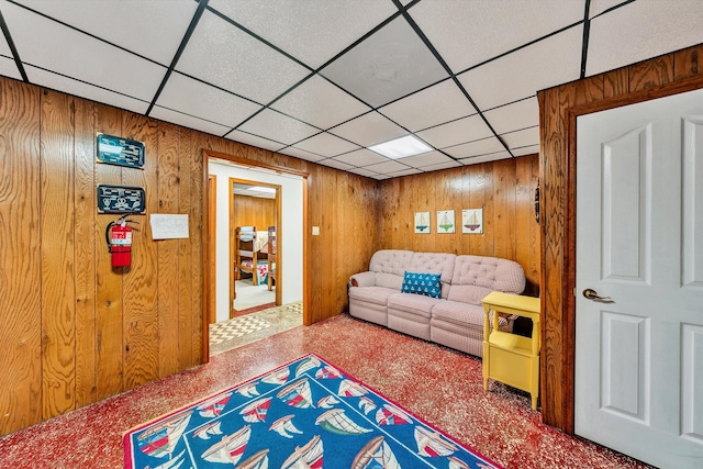 living room with a paneled ceiling and wooden walls