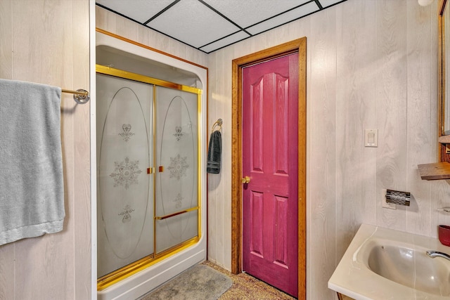 bathroom with a drop ceiling, vanity, a shower with door, and wooden walls