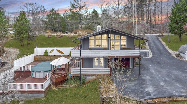 back of property at dusk featuring covered porch, fence, and driveway