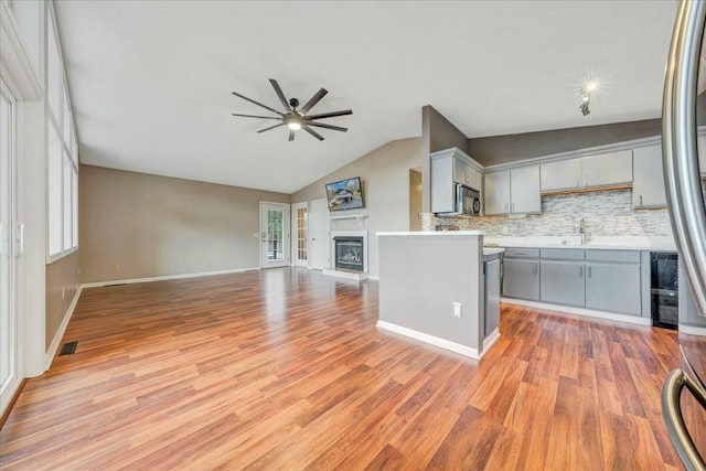 kitchen with light countertops, gray cabinetry, appliances with stainless steel finishes, a glass covered fireplace, and open floor plan